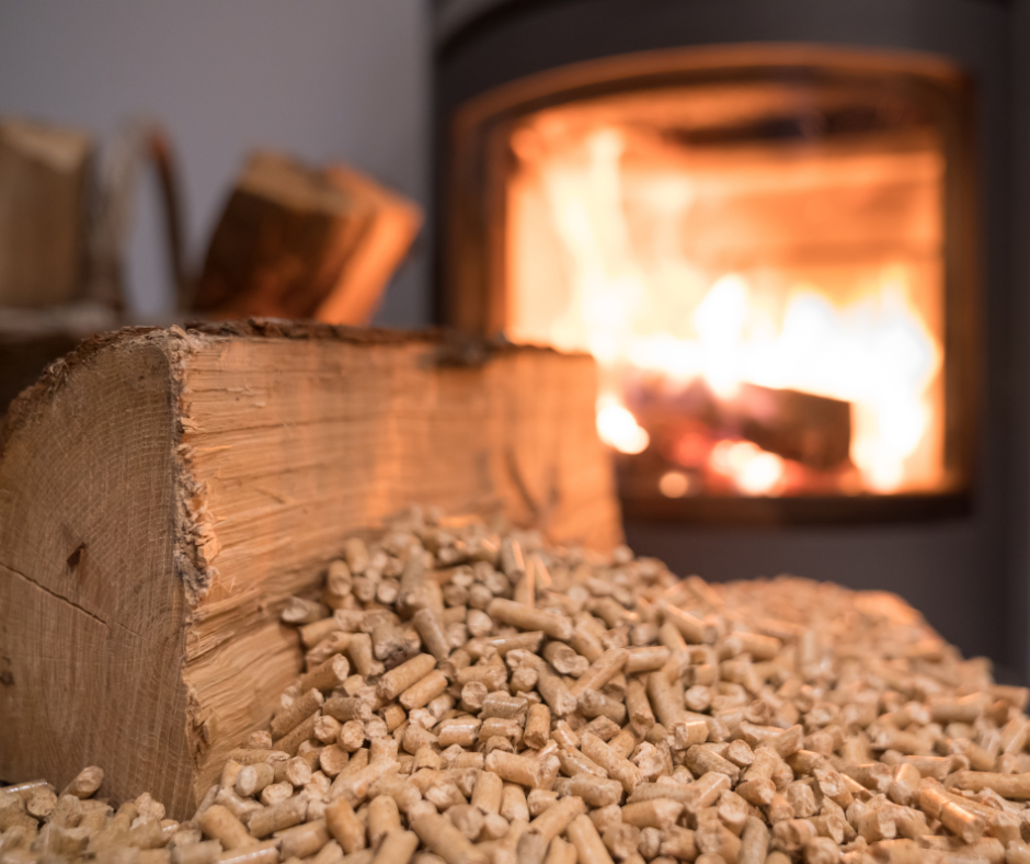 Zbliżenie na drewno opałowe i pellet drzewny przed kominkiem z płonącym ogniem w tle.
