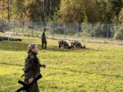 Uczennica w mundurze biegnie z karabinem podczas zawodów terenowych o charakterze wojskowym