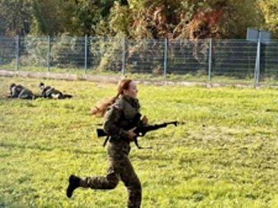 Uczennica w mundurze biegnie z karabinem podczas zawodów terenowych o charakterze wojskowym