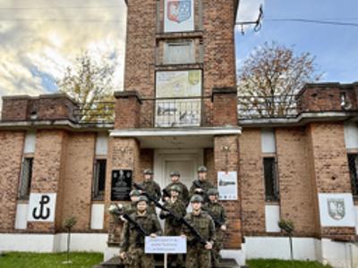 Uczniowie Zespołu Szkół im. ks. Józefa Tischnera w Dobczycach w strojach wojskowych pozują do pamiątkowego zdjęcia przed historycznym budynkiem.