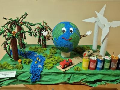 Makieta ziemi w otoczeniu zieleni, wiatraków, rzeki, koszy na śmieci oraz pojazdów