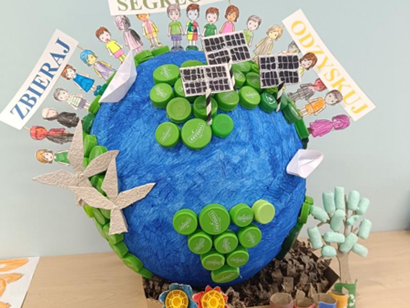 Kula ziemska z dziećmi, kontynentami z zakrętek i przykładami OZE oraz hasłami: zbieraj, segreguj, odzyskuj
