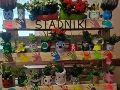 Kwietnik zrobiony z drewnianej palety z doniczkami z plastikowych butelek i metalowych puszek