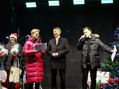 Starości stojący obok przemawiającego mężczyzny - konferansjerem oraz kobieta trzymająca dwie piłki i torby