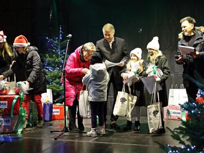 Starości wręczający na scenie nagrody 3 dzieciom, po bokach konferansjer i dwie kobiety w czapkach mikołajowych