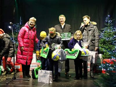 Czarna scena z choinkami, na niej starości, konferansjer, 3 dzieci trzymających nagrody i schylająca się kobieta