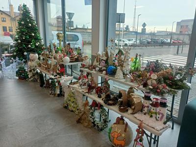 Wystawa ekologicznych ozdób świątecznych na stole i ławce, obok choinka, w tle parking widoczny przez szybę.