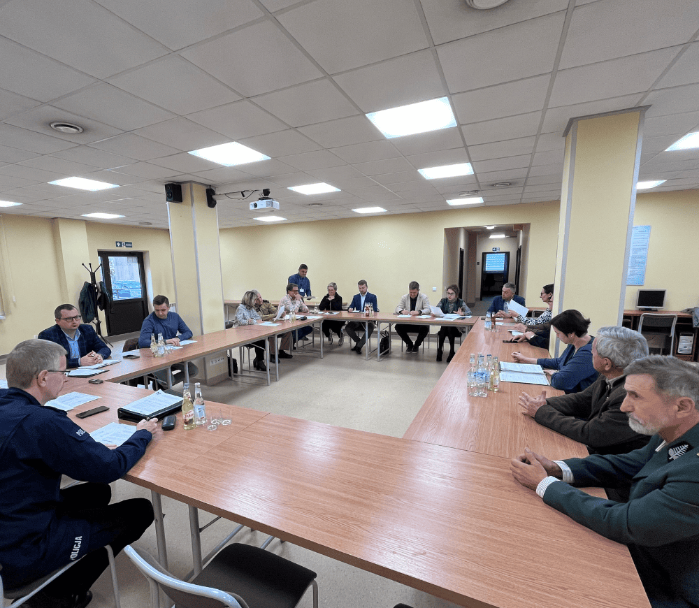 Zdjęcie z zebrania przy dużym stole w sali konferencyjnej. Uczestnicy siedzą, omawiając kwestie związane z bezpieczeństwem.