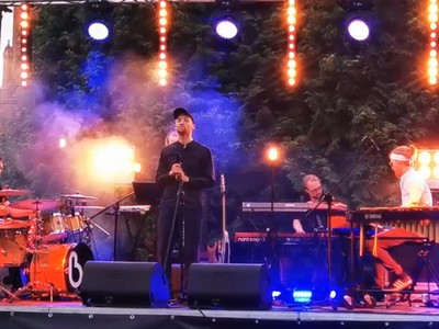 Kadr z filmu z koncertu przy katedrze. Na zdjęciu zespół na scenie i śpiewający wokalista.