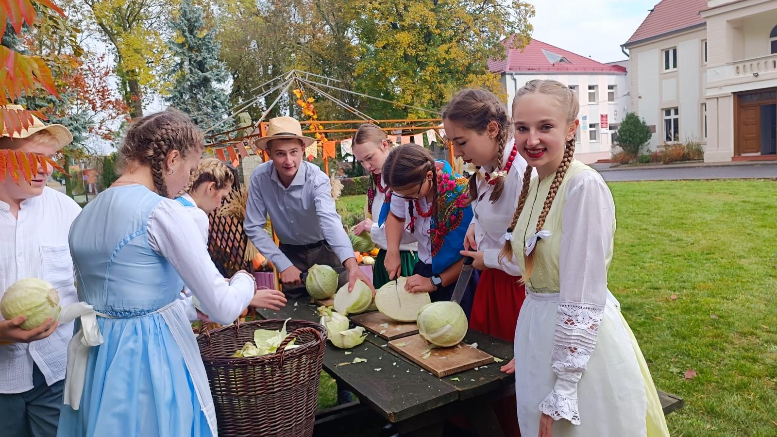 Zdjęcie przedstawia uczniów w strojach ludowych krojących kapustę.