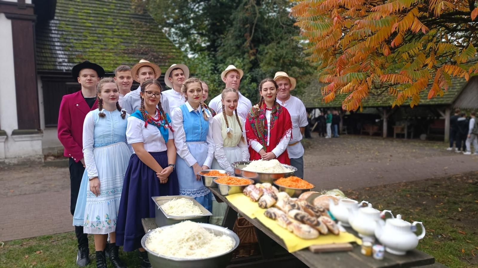 Zdjęcie przedstawia uczniów w strojach ludowych i materiały do gotowania na stole przed nimi.