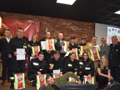 Zdjęcie przedstawia druhny i druhów z plecakami Pierwszego Ratownika i osoby je wręczające