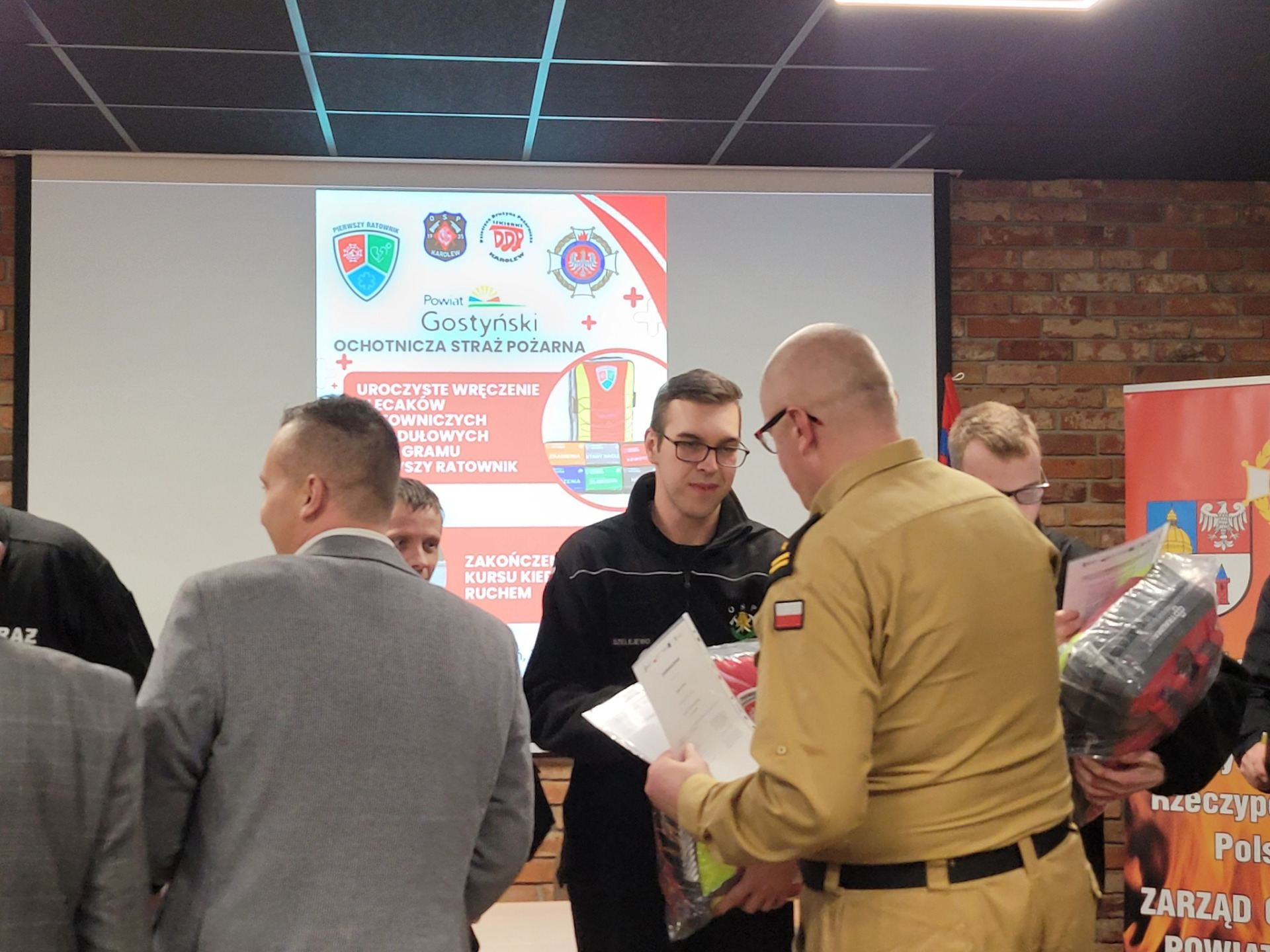 Zdjęcie przedstawia druhny i druhów z plecakami Pierwszego Ratownika i osoby je wręczające .jpg [1920x1440]