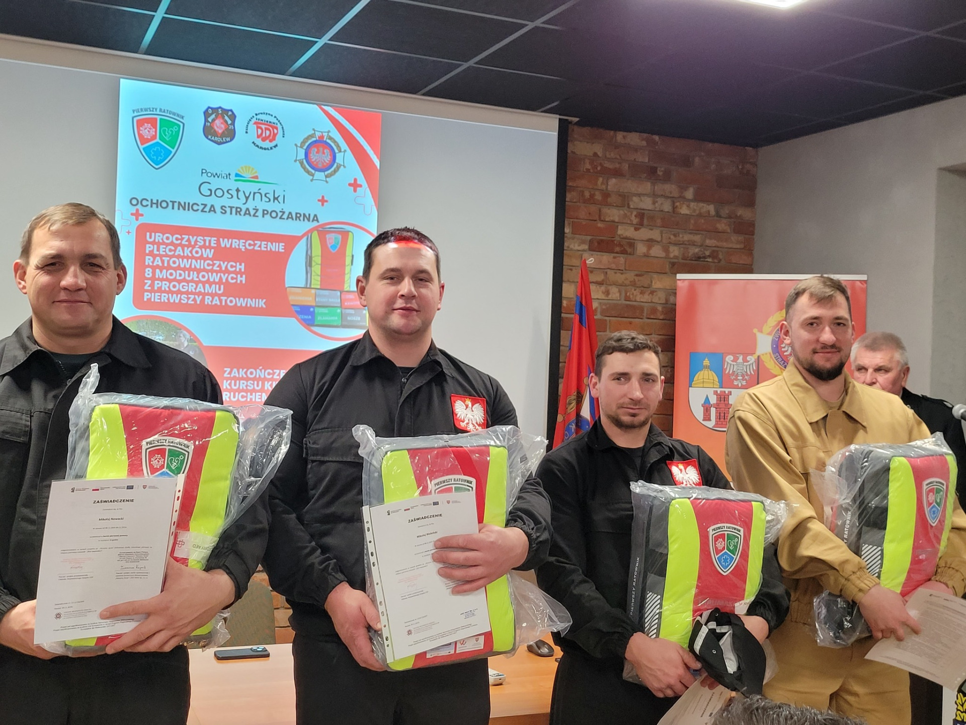 Zdjęcie przedstawia druhny i druhów z plecakami Pierwszego Ratownika i osoby je wręczające