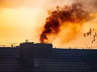 Czarny dym wydobywający się z komina domu na tle zachodzącego słońca, symbolizujący problem zanieczyszczenia powietrza.