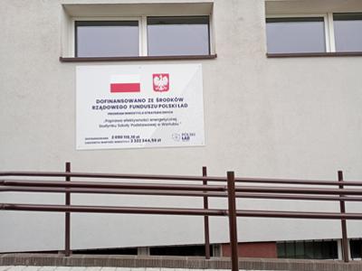 Tablica na szkole w Warlubiu informująca o dofinansowaniu inwestycji z Rządowego Funduszu Polski Ład na poprawę efektywności energetycznej.
