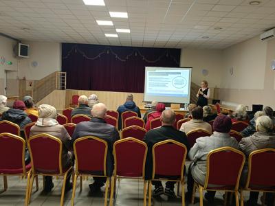 Uczestnicy spotkania siedzą na krzesłach i oglądają prezentację na sali OSP, na środku sali pracownik ZUS, spotkanie na temat tzw. wdowiej rent
