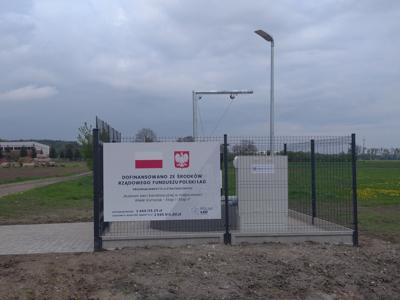 Zdjęcie przedstawia ogrodzenie przepompowni wraz z tablicą z napisem