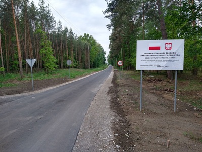 Otwarcie drogi gminnej w miejscowości Płochocin, zdjęcie drogi + tablica "Dofinansowano ze środków państwowego funduszu celowego"