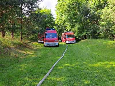 Ćwiczenia OSP, trzy wozy strażackie, na środku kadru przebiega wąż strażacki