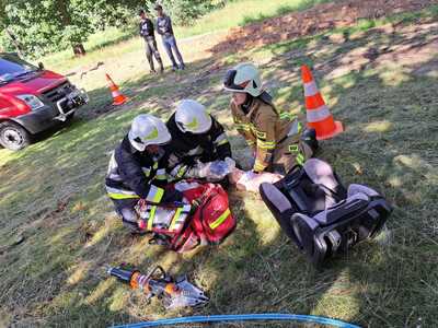 Ćwiczenia OSP, dwóch strażaków wyjmuje z torby wyposażenie, trzeci strażak kobieta przy manekinie do udzielania pierwszej pomocy