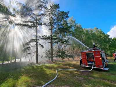 Ćwiczenia OSP, wóz strażacki na tle drzew w obszarze leśnym, z wozu strażackiego puszczana jest woda