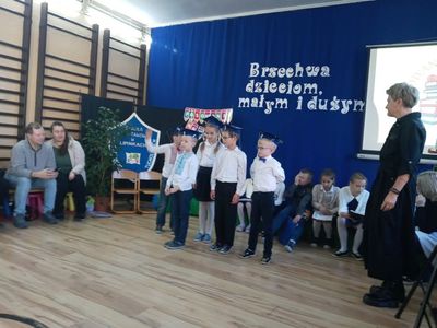 Dzień Edukacji Narodowej w SP Lipinki. Dzieci na tle dekoracji, w tle rodzice, nauczyciele i szkolny sztandar