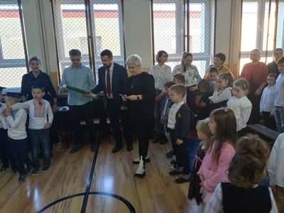 Uczniowie i nauczyciele podczas uroczystości szkolnej, chłopiec w stroju ludowym pasowany na ucznia dużym ołówkiem
