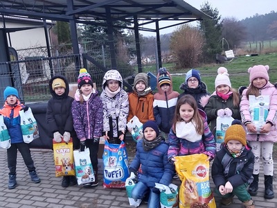 SP Wielki Komorsk wspiera schronisko dla zwierząt. Grupa dzieci w zimowych ubraniach z karmą dla zwierząt przed schroniskiem