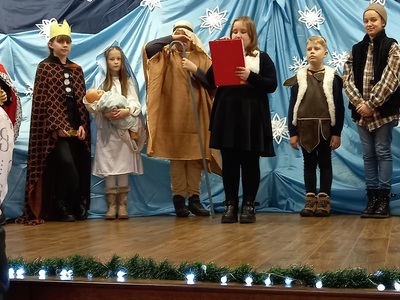 Wigilia dla osób starszych i samotnych w SP Wielki Komorsk. Dzieci w strojach biblijnych odgrywają scenę jasełek na tle dekoracji z gwiazdkami