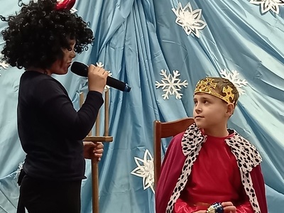 Wigilia dla osób starszych i samotnych w SP Wielki Komorsk. Dzieci w kostiumach podczas jasełek – diabeł rozmawia z królem na tle zimowej dekoracji