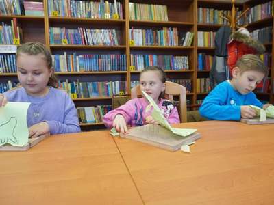 dzieci w bibliotece, siedzą przy stole i wycinają wycinanki