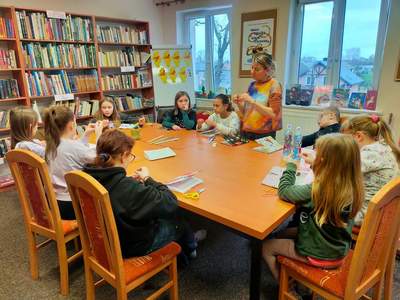 dzieci w bibliotece, siedzą przy stole i wycinają wycinanki