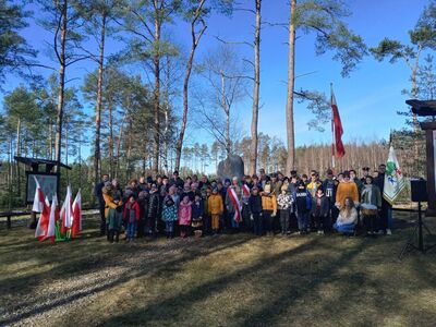 Święto Żołnierzy Niezłomnych w Lipinkach, Grupowe zdjęcie uczniów i dorosłych przy pomniku w lesie, z flagami i pocztami sztandarowymi
