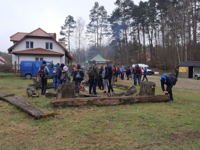 Warlubskie XVI Marsze na Orientację „BIELOWSZCZAK” 2023. Uczestnicy Marszów na Orientację przy ognisku na polanie, z namiotem i zabudowaniami w tle
