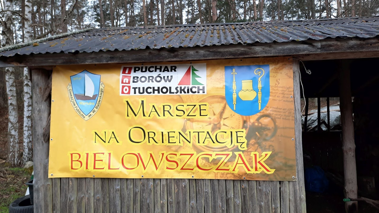 Baner Marszów na Orientację "Bielowszczak" w Borach Tucholskich na drewnianej wiacie, z herbami i logotypem wydarzenia