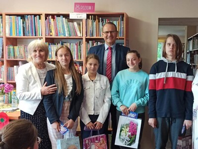 podsumowanie konkursu "Pożeracze książek", wójt gminy, przewodnicząca gminy, dzieci w bibliotece na tle regałów z książkami