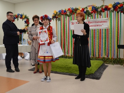 Dziewczyna w stroju ludowym odbiera dyplom i nagrodę podczas konkursu recytatorskiego