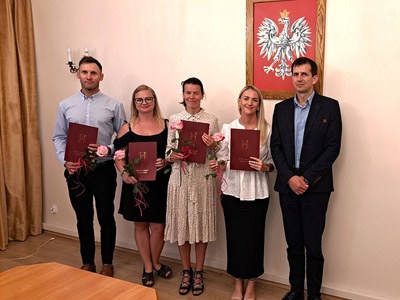 Nauczyciele mianowani trzymają róże i teczki z herbem gminy, na zdjęciu z Wójtem Gminy Mariuszem Kosikowskim