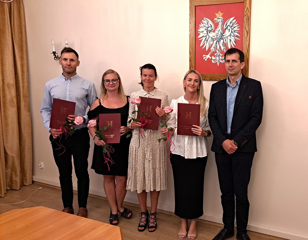 Nauczyciele mianowani trzymają róże i teczki z herbem gminy, na zdjęciu z Wójtem Gminy Mariuszem Kosikowskim