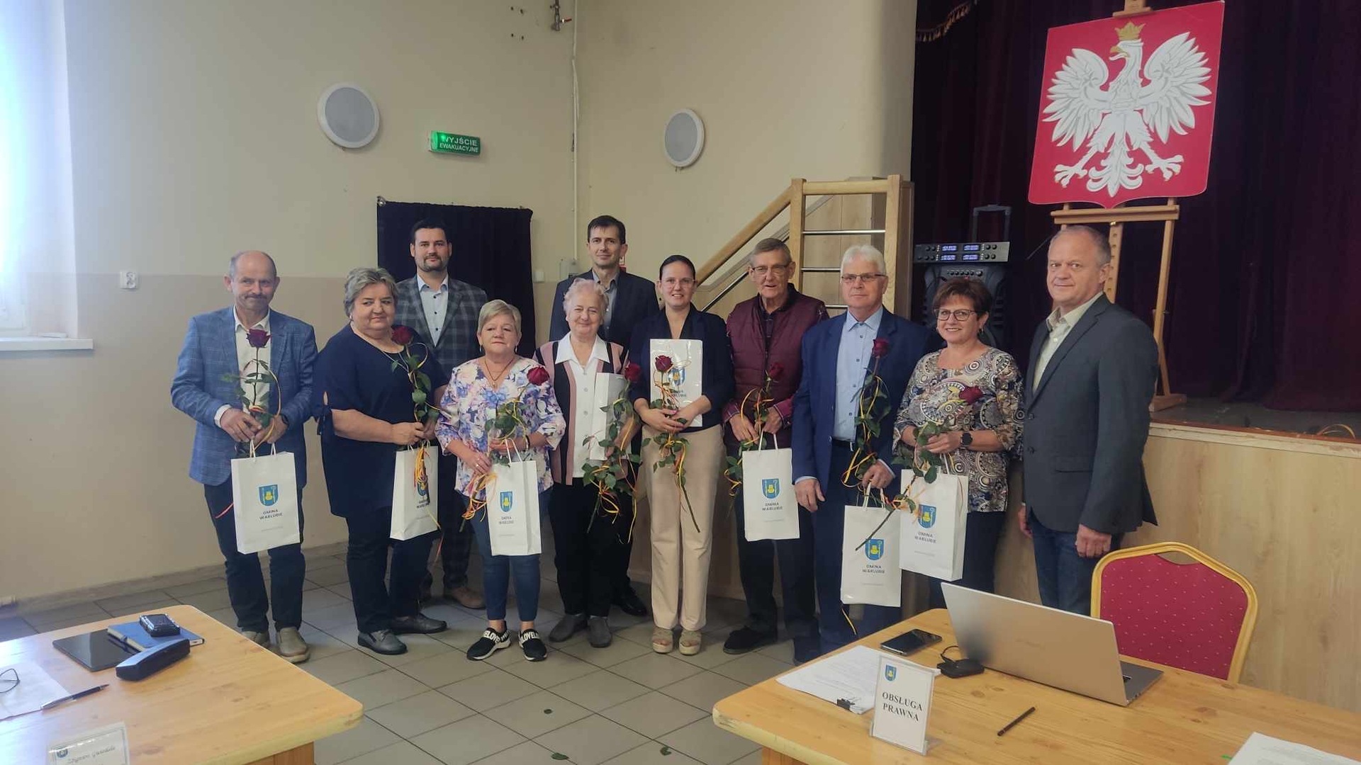 Pożegnanie sołtysów. Wójt, Przewodniczący, Sołtysi z różami i torbami z herbem gminy Warlubie podczas uroczystości w sali OSP