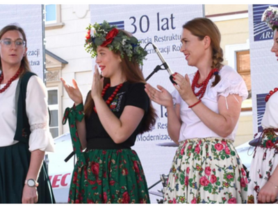 Cztery kobiety w strojach ludowych na scenie w tle baner i mikrofony