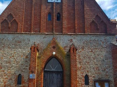 Zdjęcie przedstawia główne wejście do kościoła w Malechowie wraz z zegarem.