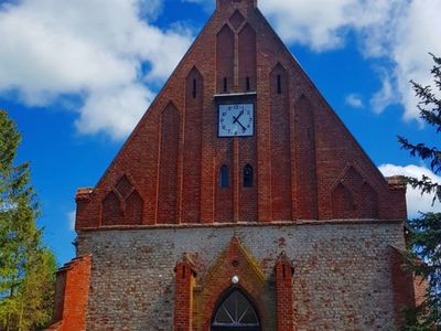 Zdjęcie przedstawia główne wejście do kościoła w Malechowie wraz z zegarem.