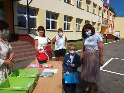 Zdjęcie przedstawia przedszkolaka z mamą i grono pedagogiczne ZS Ostrowiec podczas zakończenia roku szkolnego. 