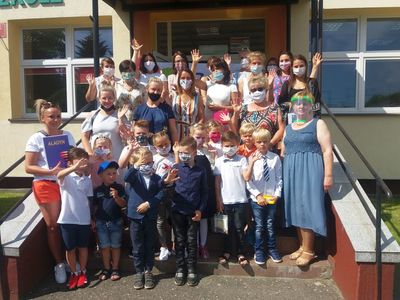 Zdjęcie przedstawia grupę przedszkolaków, rodziców i grono pedagogiczne Zespołu Szkół w Ostrowcu podczas zakończenia roku szkolnego. 