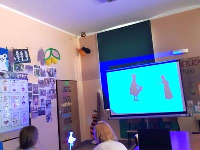 Zdjęcie przedstawia dziecko i wychowawczynię obserwujące teatr cieni na tablicy interaktywnej.