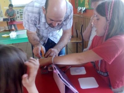 Zdjęcie przedstawia dwie dziewczynki z nauczycielem podczas zajęć z robotyki. 
