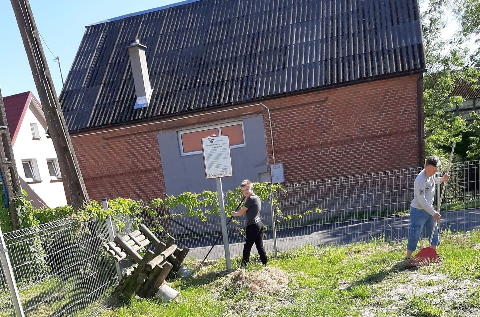 Zdjęcie przedstawia dwóch chłopców porządkujących teren przy świetlicy w Przystawach.