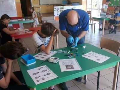 Zdjęcie przedstawia wychowanków Placówki Wsparcia Dziennego w Laskach z nauczycielem, którzy konstruują robota miotającego.